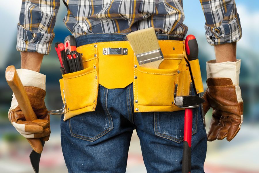 Tradesman from behind wearing a yellow tool belt with a paintbrush, hammer and screwdrivers