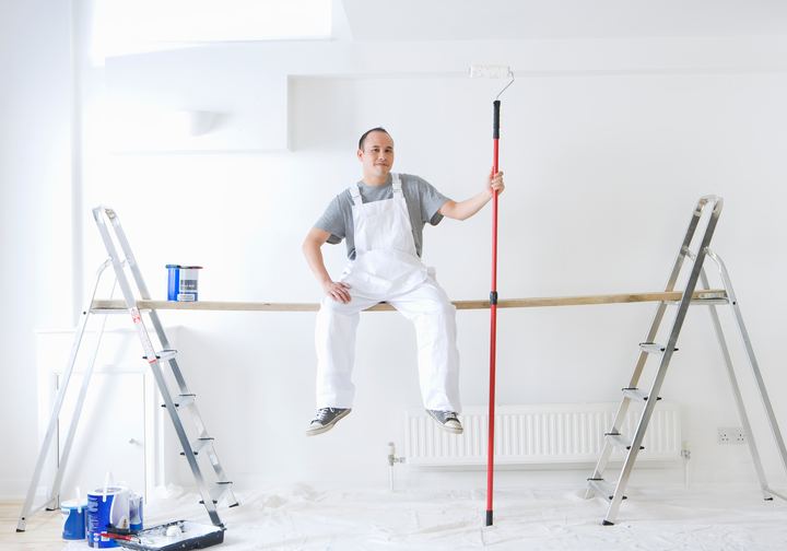 Painter sitting on a scaffold plank holding a paint roller
