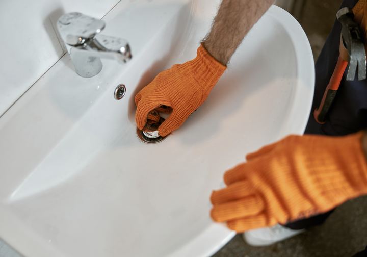 Gloved hands fixing a bathroom sink drain